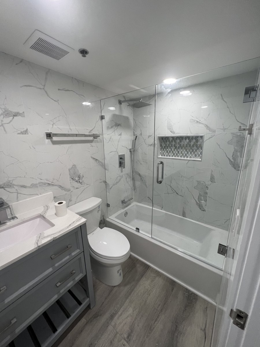 Bathroom remodel by KM — marble-look tile, glass-enclosed tub and shower, and gray vanity